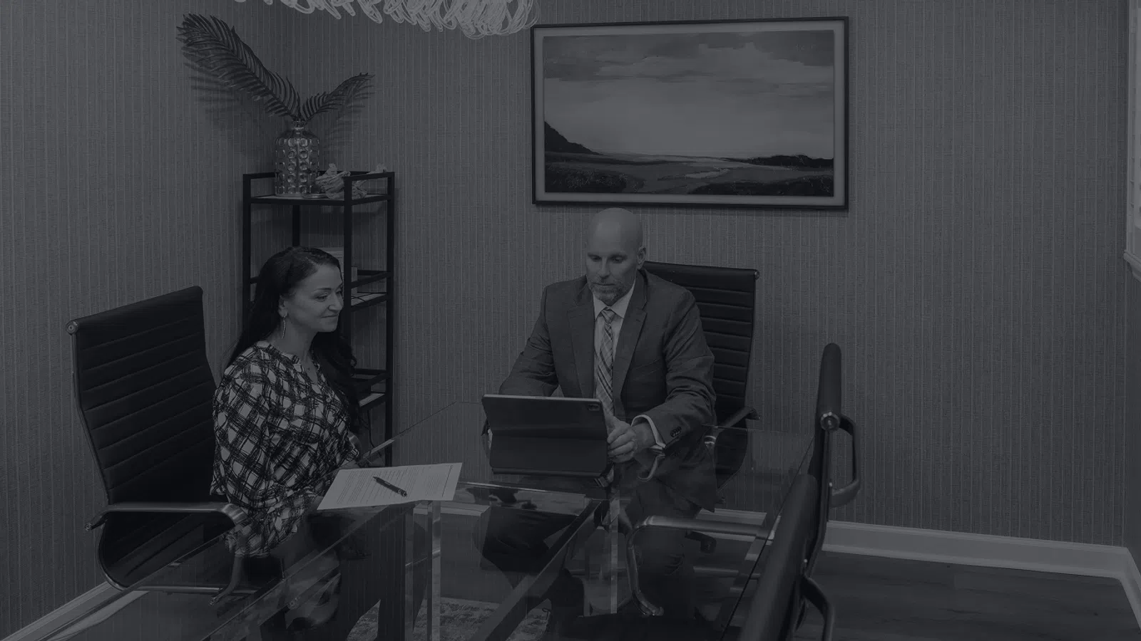 Two professionals in a modern office having a business meeting with laptop and documents on glass table.