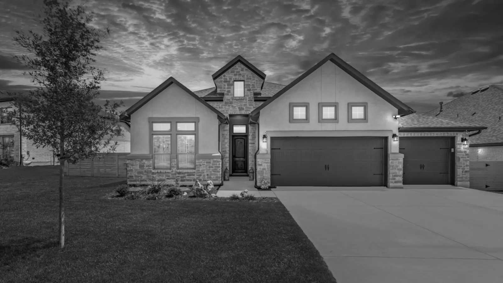 Modern suburban house with three-car garage, stone accents, and dramatic cloudy evening sky.