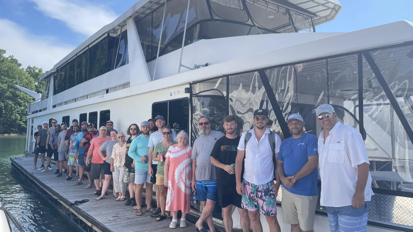 Group of people lined up on a dock next to a large white boat under clear blue sky.