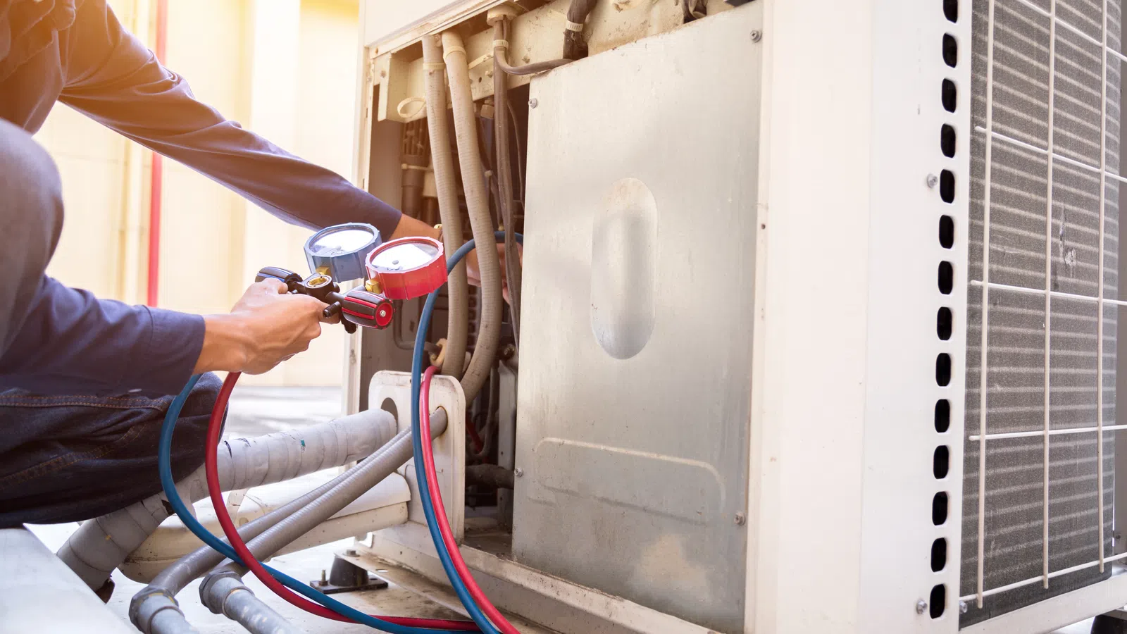Technician servicing an air conditioning unit using gauges and hoses to check performance and repairs.