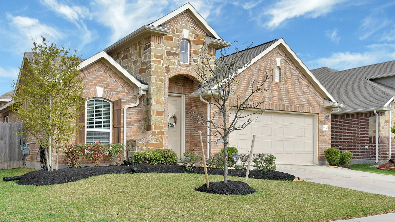 Modern single-story brick house with stone accents, a two-car garage, young trees, and a green lawn under a blue sky