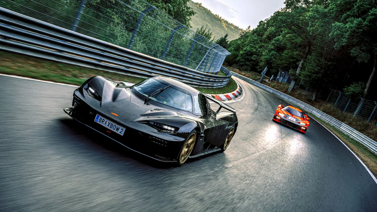 Black and orange race cars speeding on a curved forested race track during daylight.