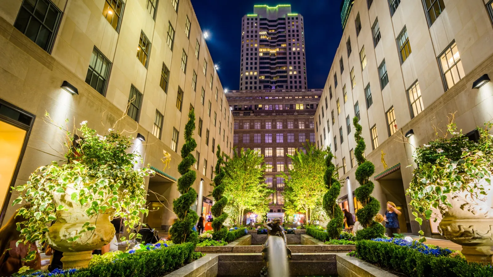 a courtyard with plants and trees in it with buildings in the back with Rockefeller Center in the background