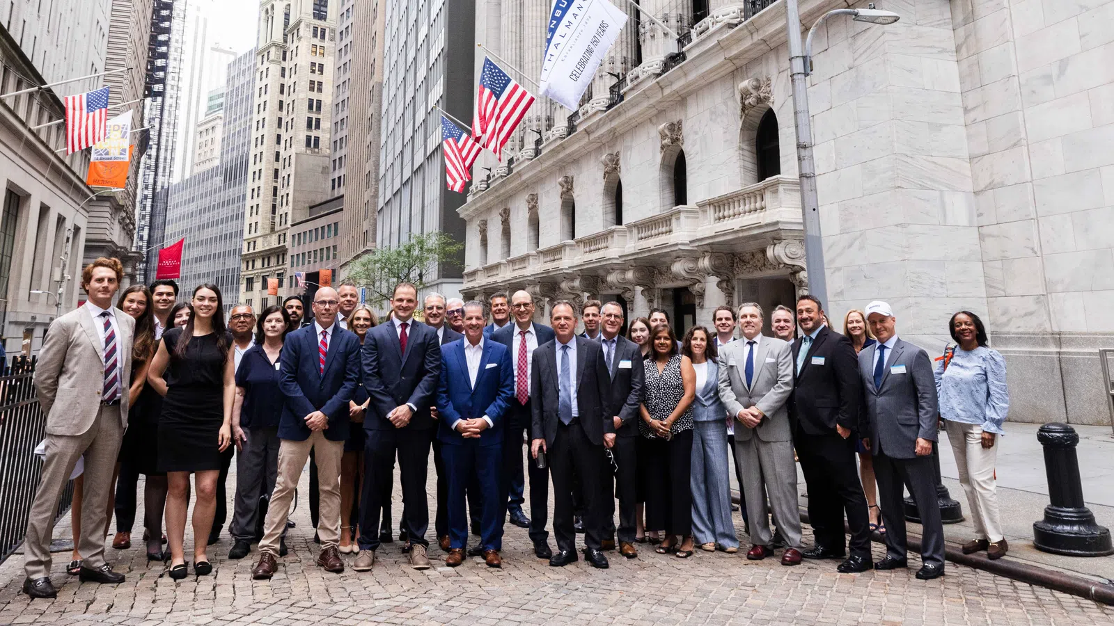 Group of professionals in business attire posing on Wall Street in New York City near the stock exchange building.