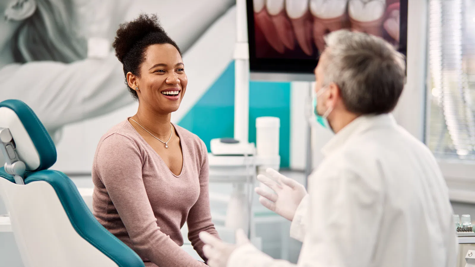 Smiling woman sitting in dental chair talking to dentist in clinic during consultation.