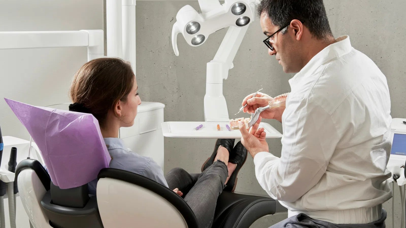 Dentist demonstrating dental model to patient seated in dental chair in modern clinic
