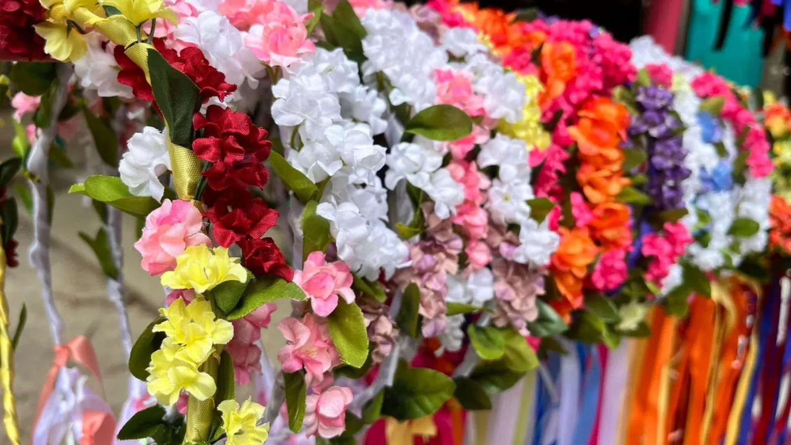 Colorful artificial flower garlands with green leaves and hanging ribbons arranged in a row.