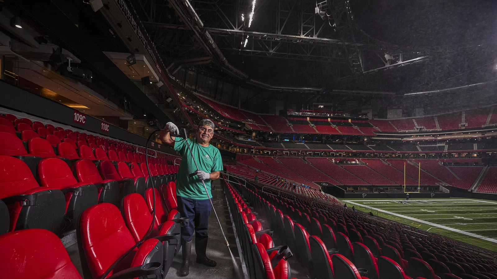 Worker wearing green shirt sprays disinfectant in empty stadium seating before event