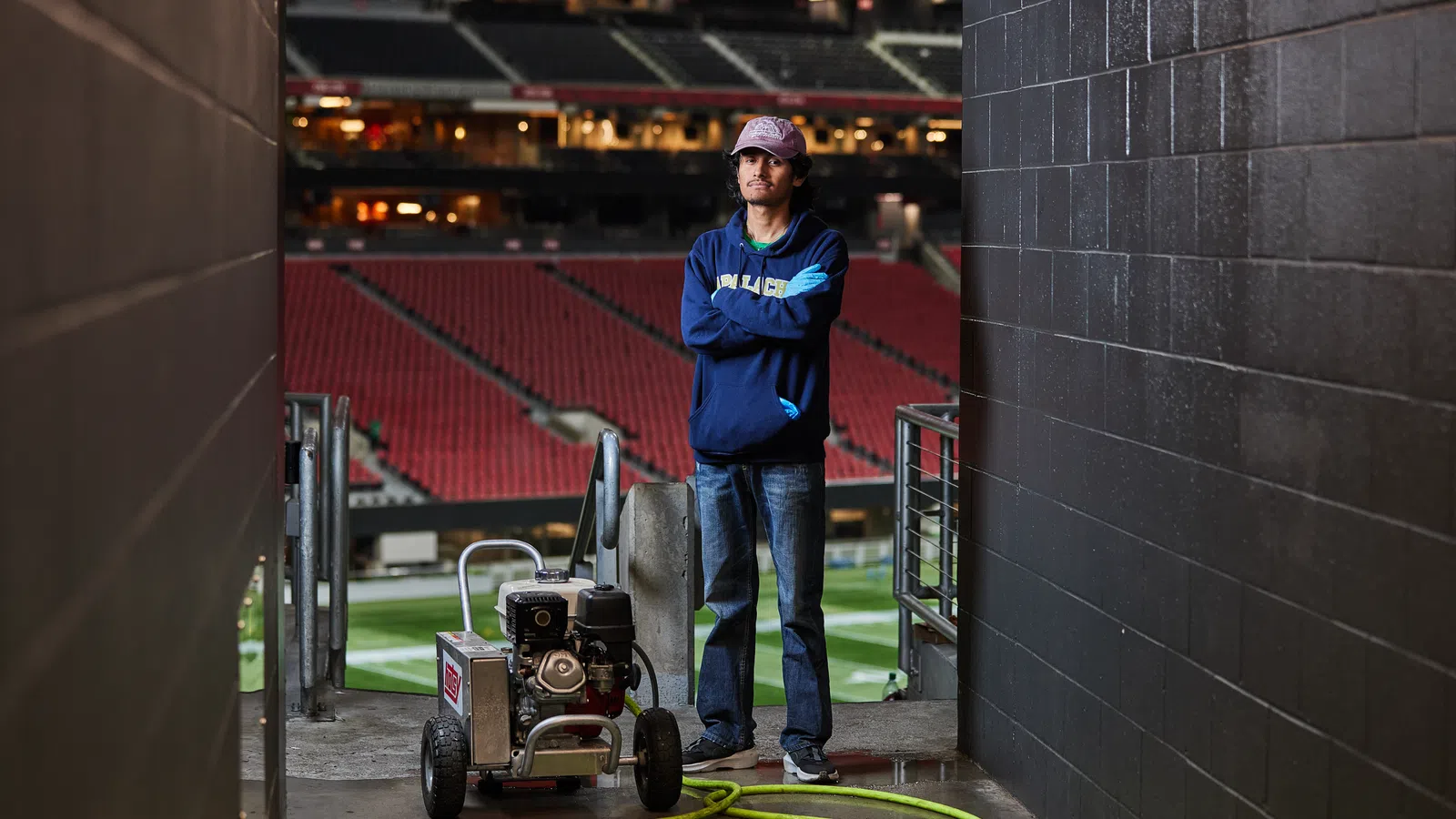 Man in casual clothes standing in a stadium tunnel with turf maintenance equipment and coiled hose.