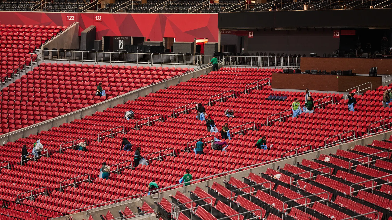 Rows of red stadium seats with scattered people spaced apart during an event or game preparation.