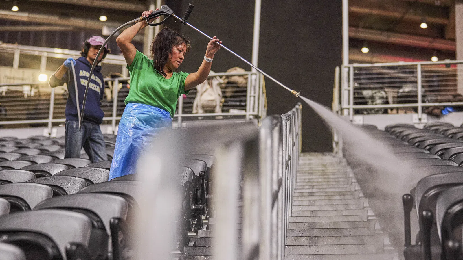 Workers cleaning stadium seats and aisles with pressure washers during maintenance.