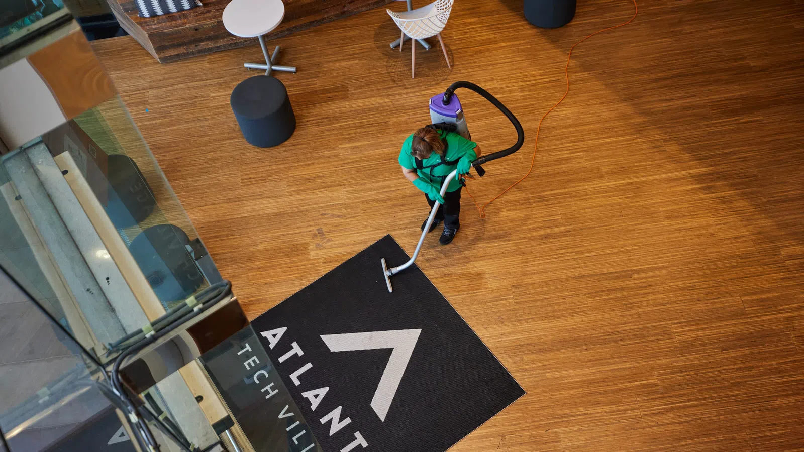 Person cleaning a black Atlanta Tech Village floor mat on wooden floor in modern office lobby