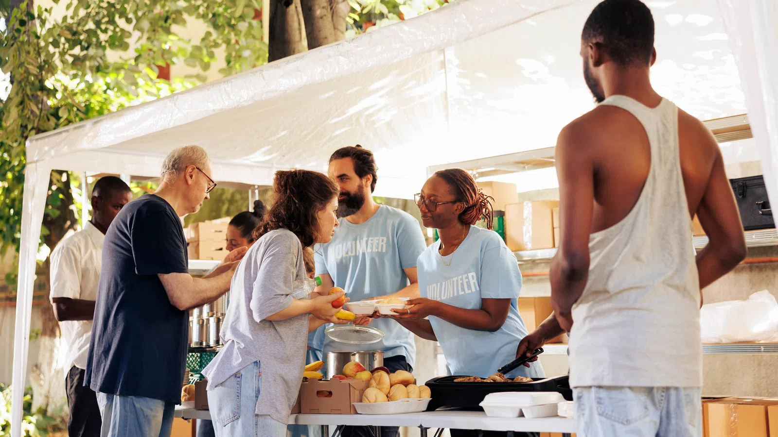 Volunteers serving food and handing out bread to people at an outdoor community food distribution event.