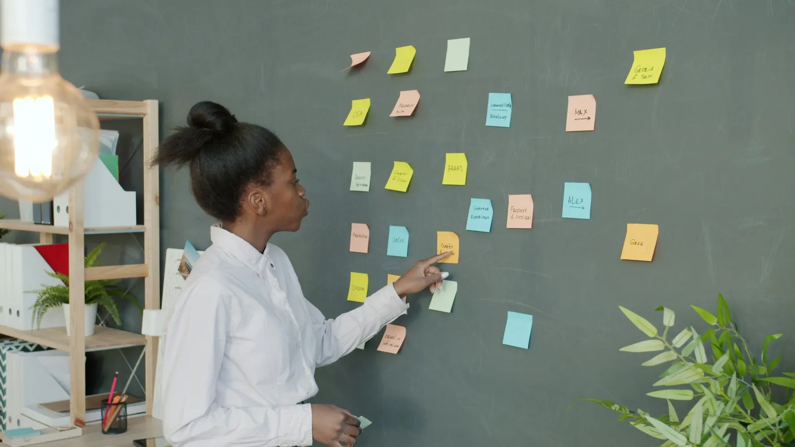 Woman organizing colorful sticky notes on a chalkboard in a modern office setting