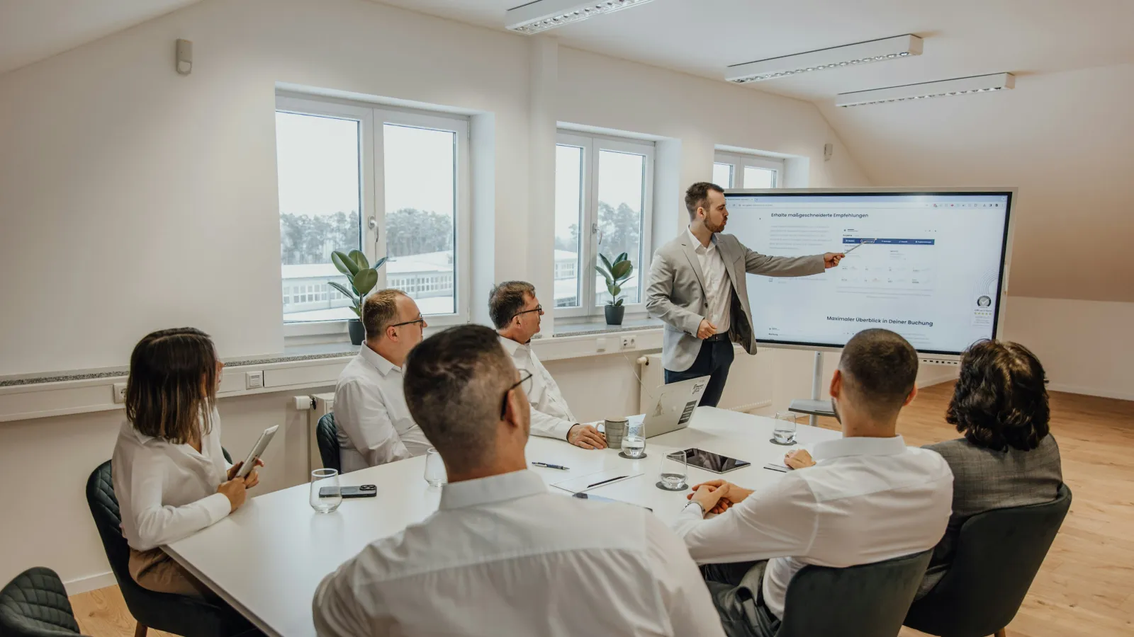 Business team attending presentation in modern meeting room with large screen and laptops.