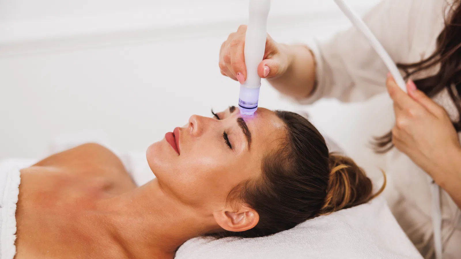Woman receiving advanced facial treatment with a handheld device on forehead in a spa setting