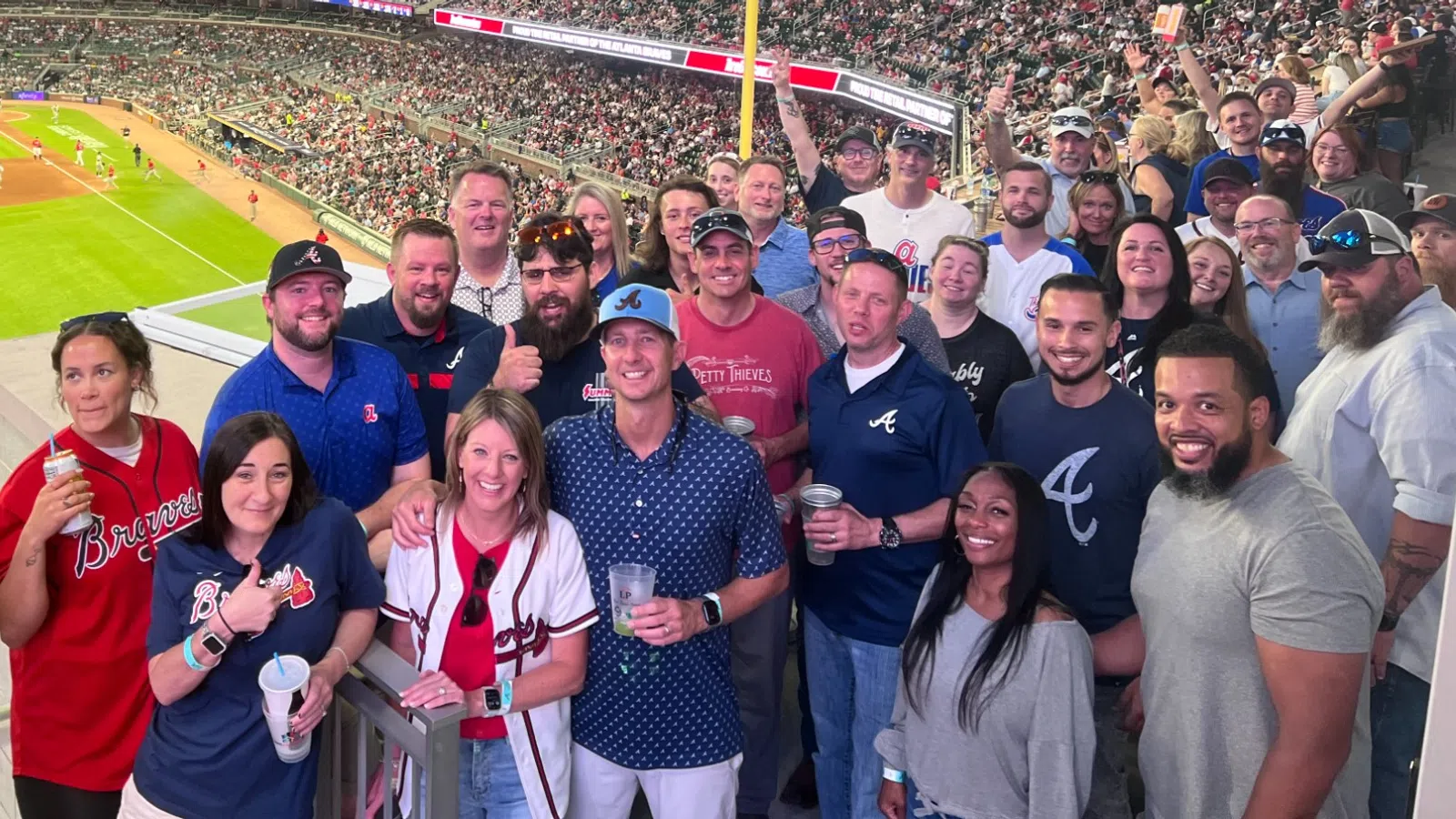 Group of fans enjoying a baseball game at a crowded stadium with bright lights and field view.