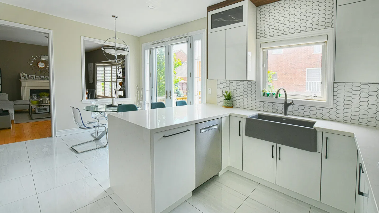 Modern white kitchen with large island, farmhouse sink, tile backsplash, and glass dining table in bright open space