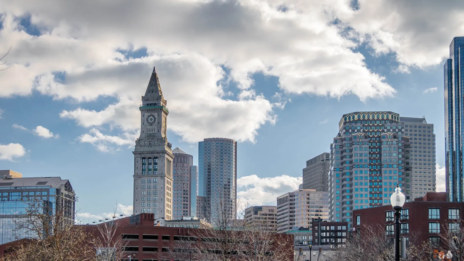 Skyline of Boston featuring the Custom House Tower, modern skyscrapers, and a partly cloudy sky.