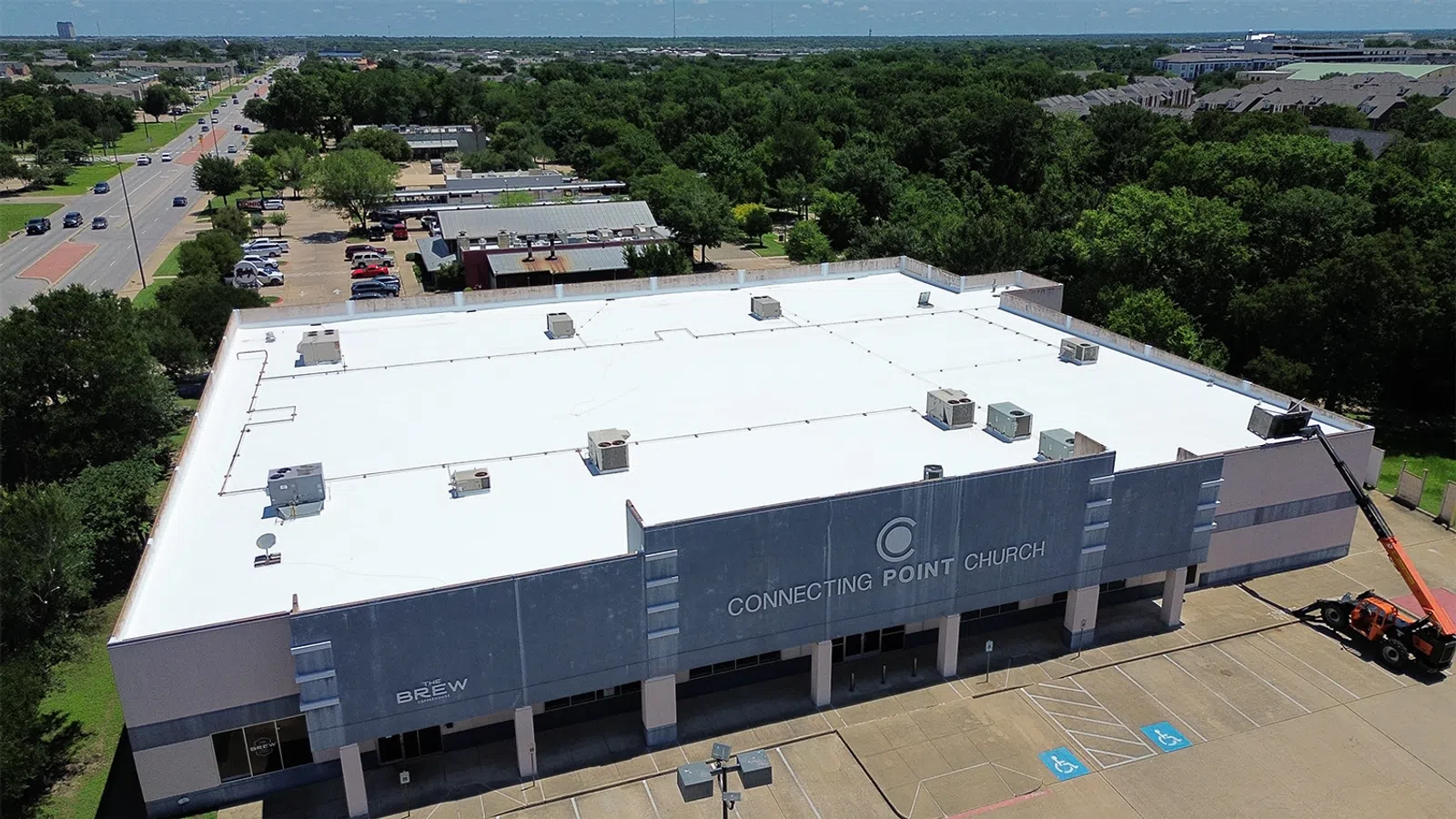 Aerial view of Connecting Point Church building with parking lot, surrounding trees, and nearby roads on a sunny day