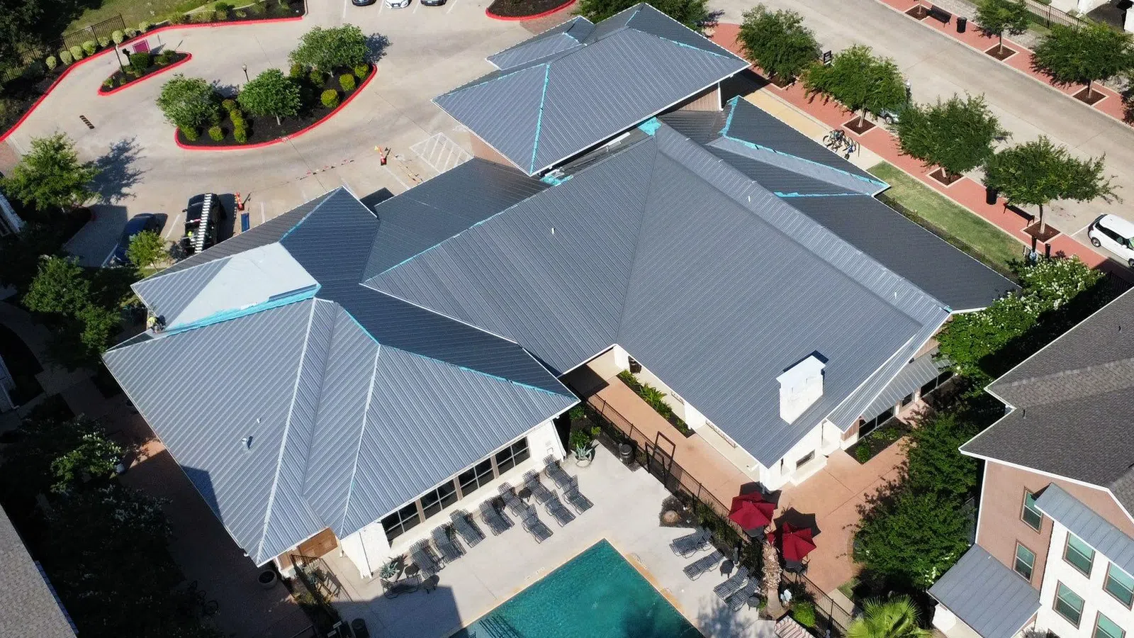Aerial view of a residential complex with a swimming pool, parking area, and multiple buildings with metal roofs.