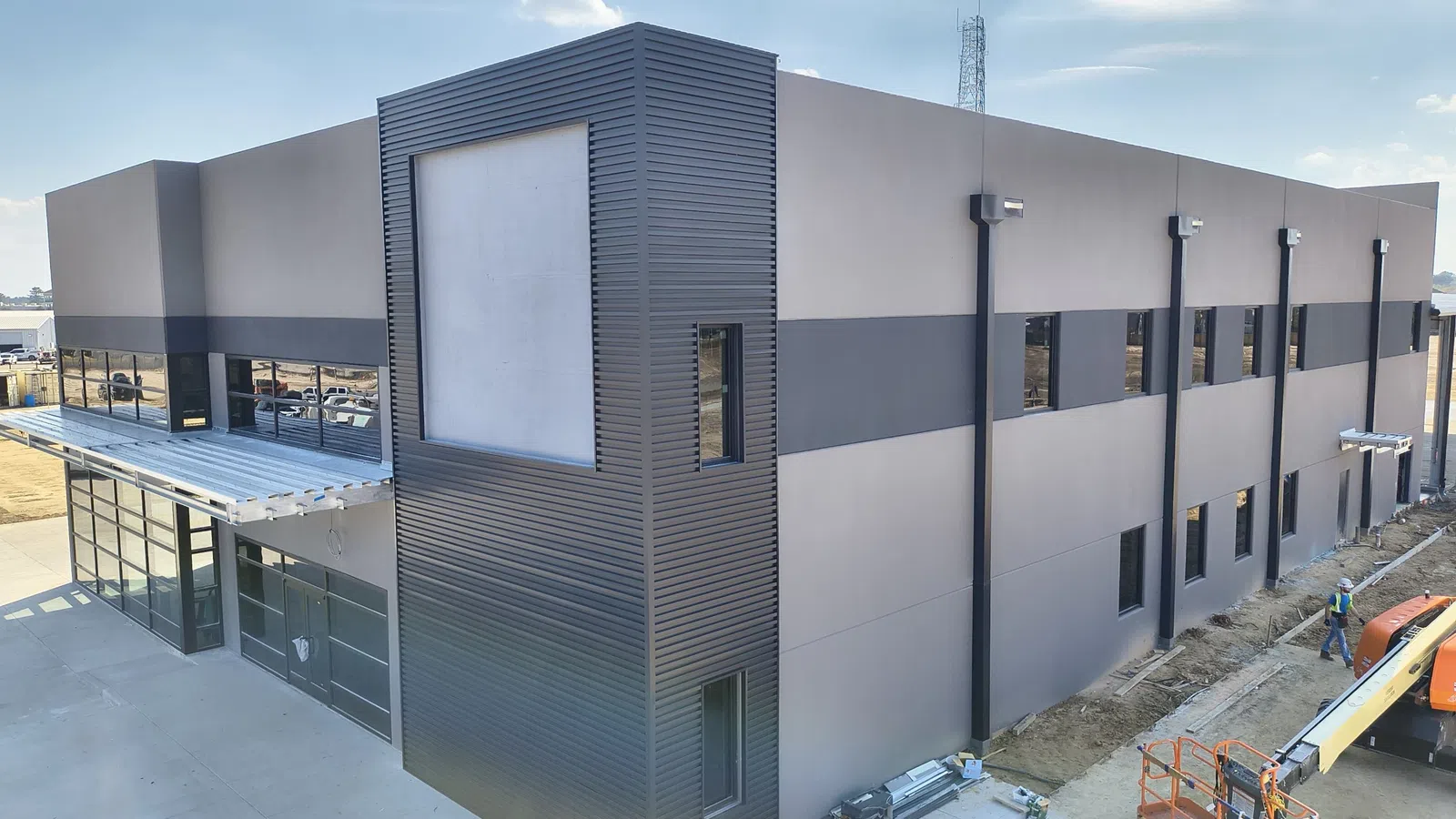 Exterior view of a newly constructed two-story commercial and industrial building in the Houston area featuring modern metal panel and stucco facade with a new roofing system, under final construction with a Mattco crew member on site.