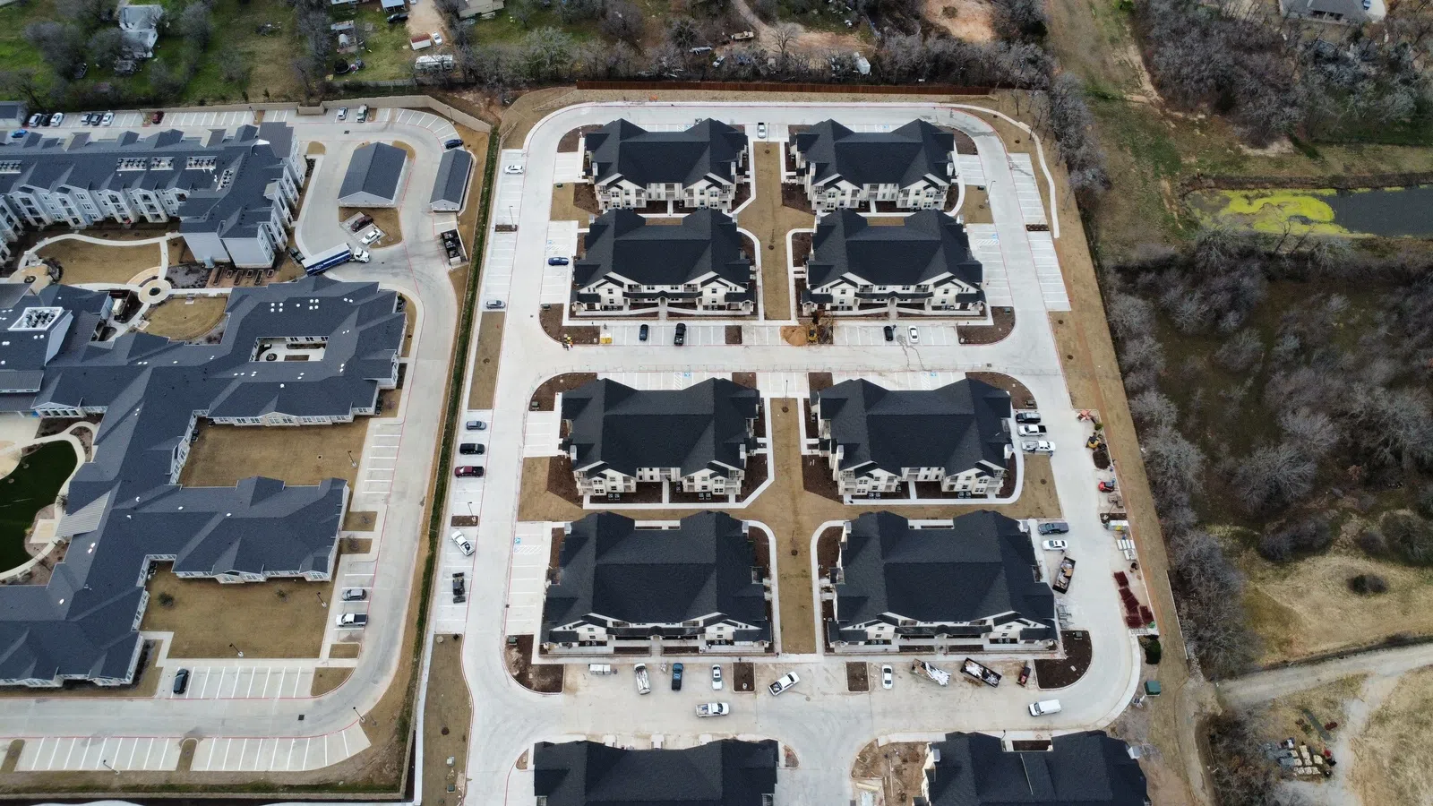 Aerial view of new architectural shingle roofing on a multi-family residential community under construction in the Dallas-Fort Worth area, showing completed roof sections across townhome-style buildings with stone and siding exteriors.
