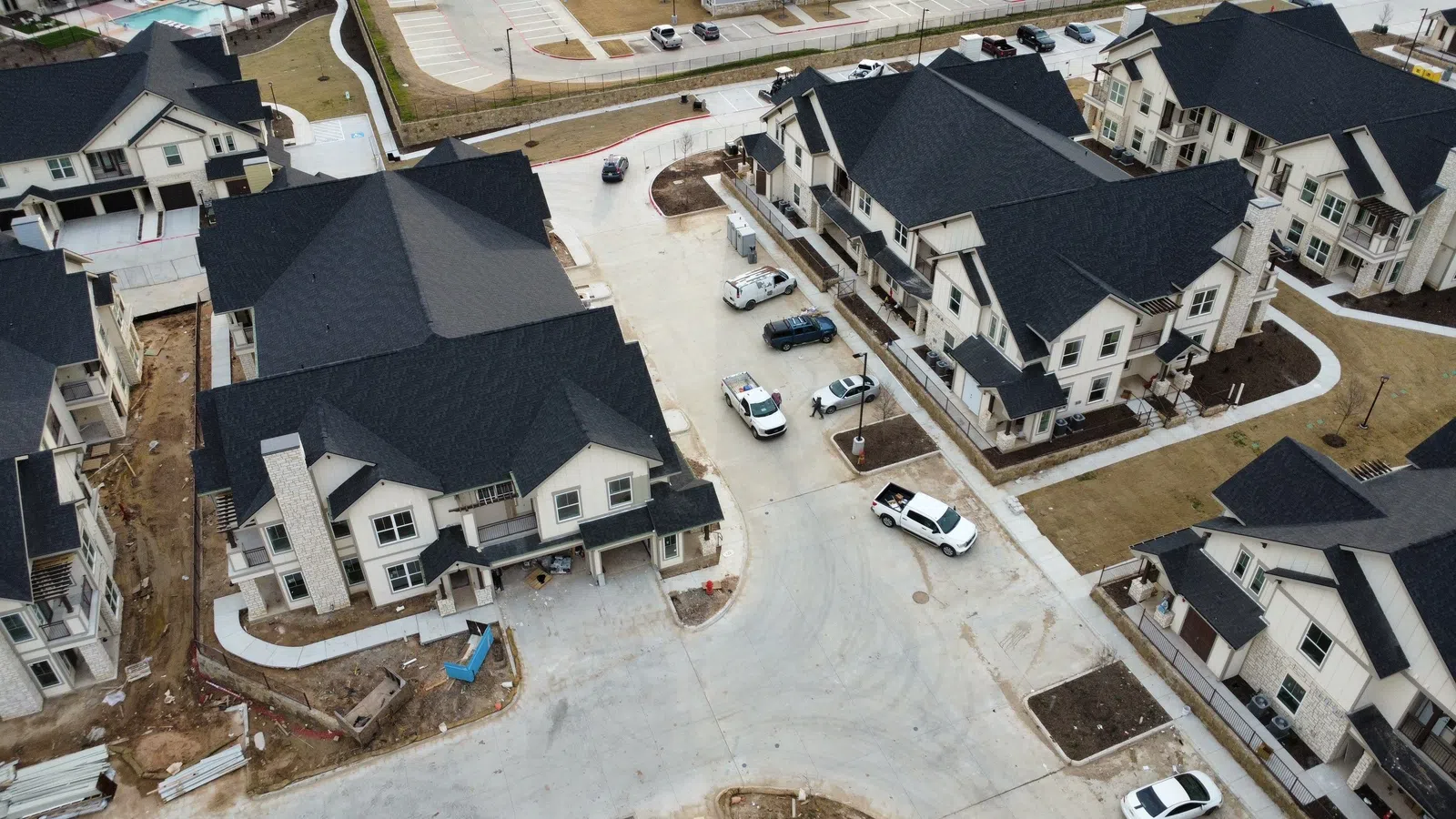 Aerial view of a completed multi-family apartment community in the Dallas-Fort Worth area with new architectural shingle roofing installed across multiple three-story residential buildings, alongside an adjacent senior living community.