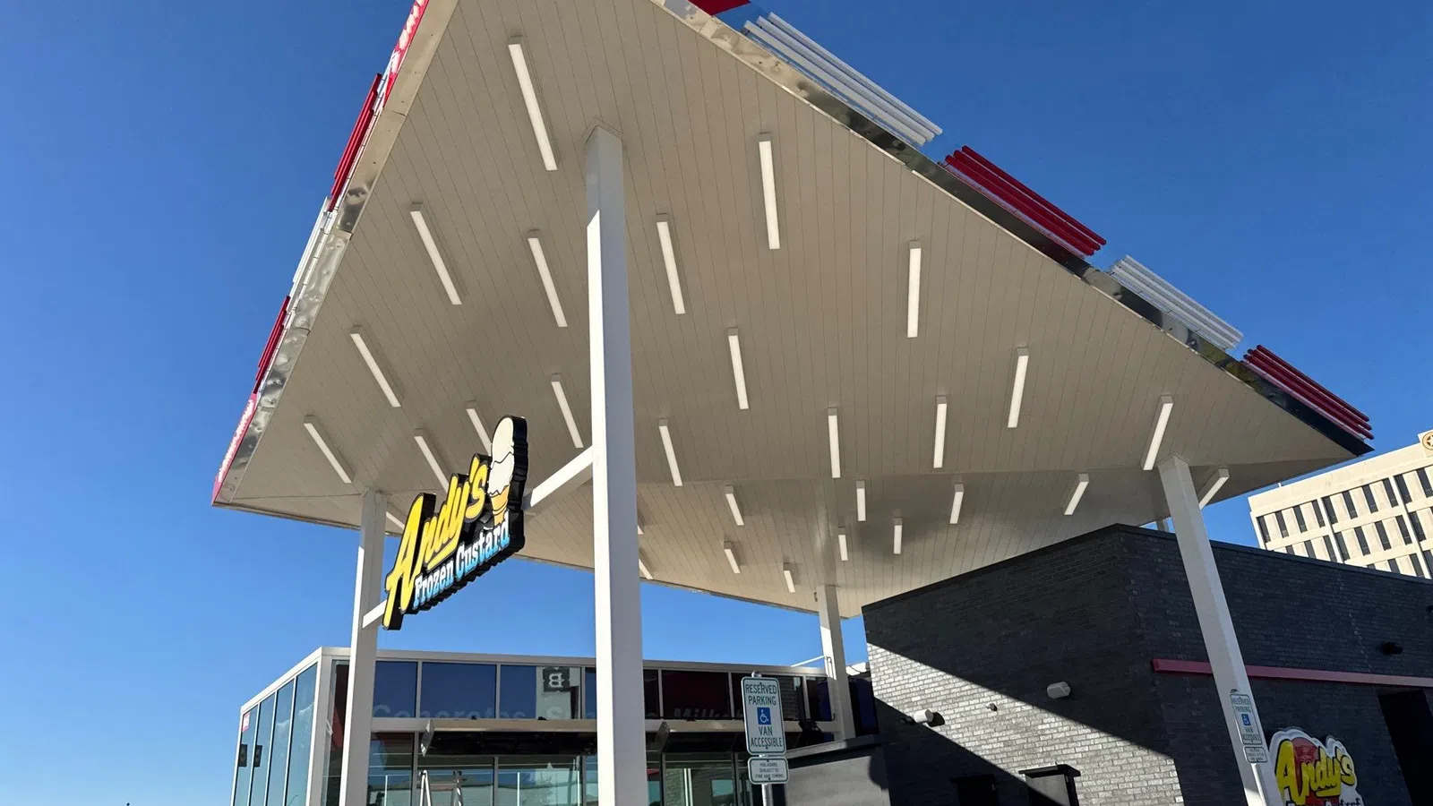 Low-angle view of a completed standing seam metal drive-thru canopy roof on an Andy's Frozen Custard restaurant in the Dallas-Fort Worth area, showing the finished underside with integrated lighting against a clear blue sky.