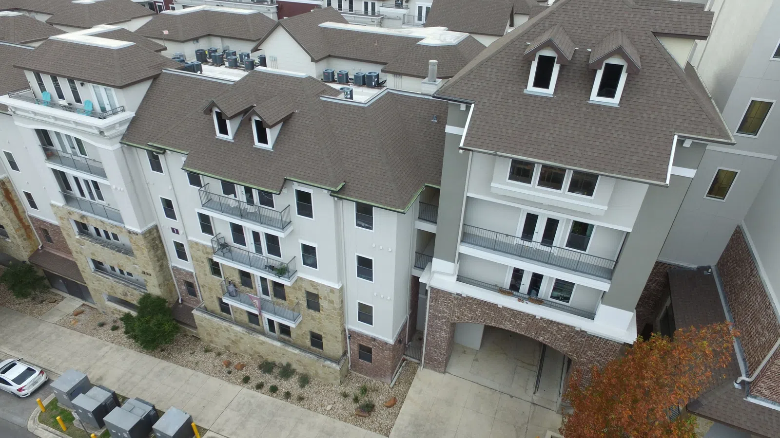 Aerial view of a completed architectural shingle roof on a multi-family student housing community in Austin, Texas, featuring steep gabled and dormered rooflines across multiple connected residential buildings with stone and stucco exteriors.