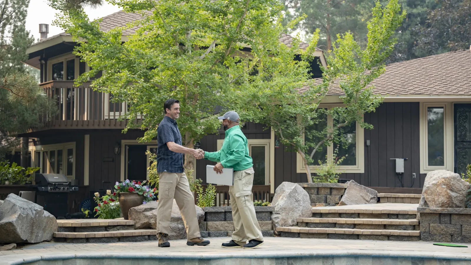 a couple of men standing by a pool in front of a house