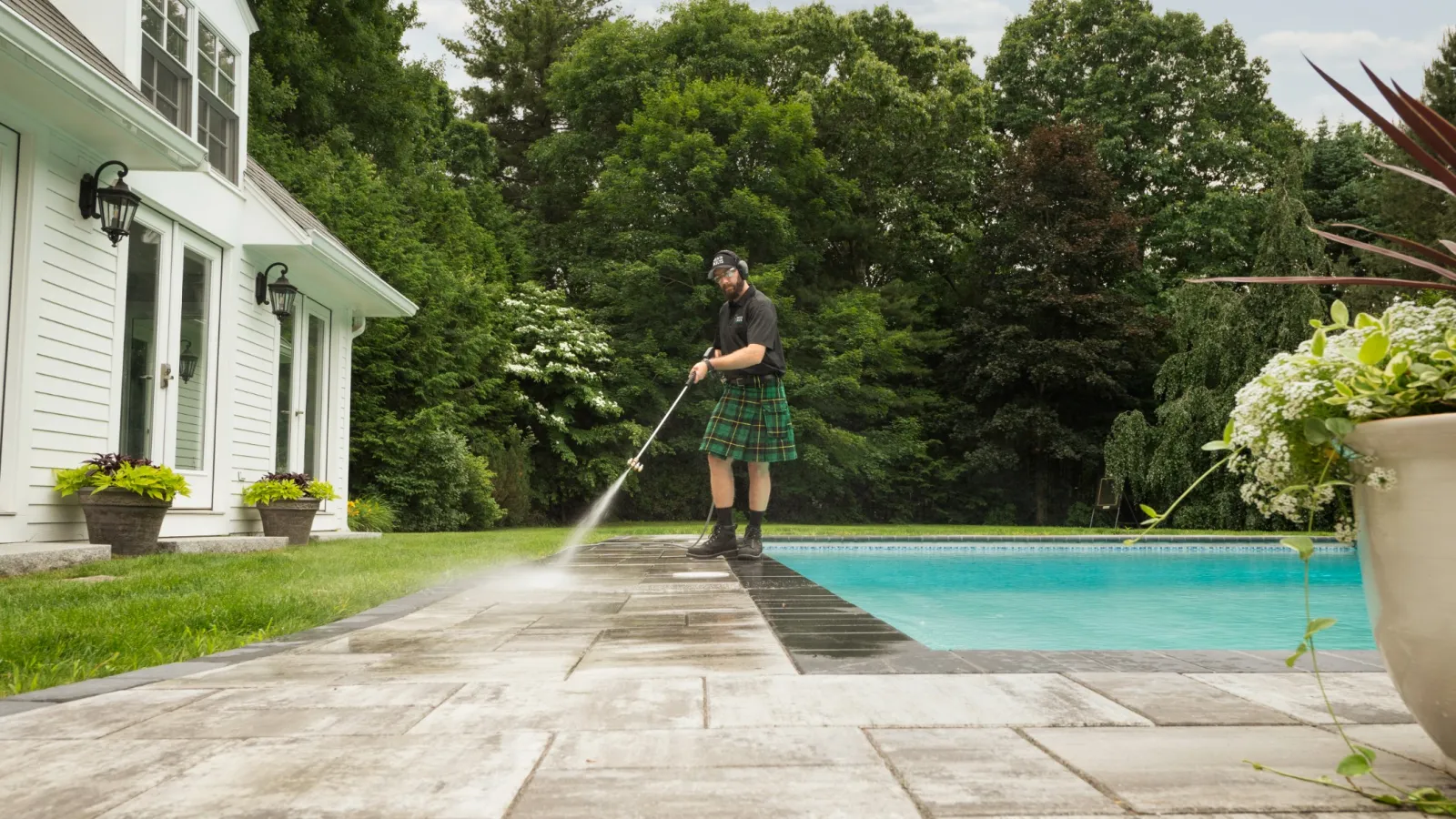 a man in a kilt pressure washing beside a pool