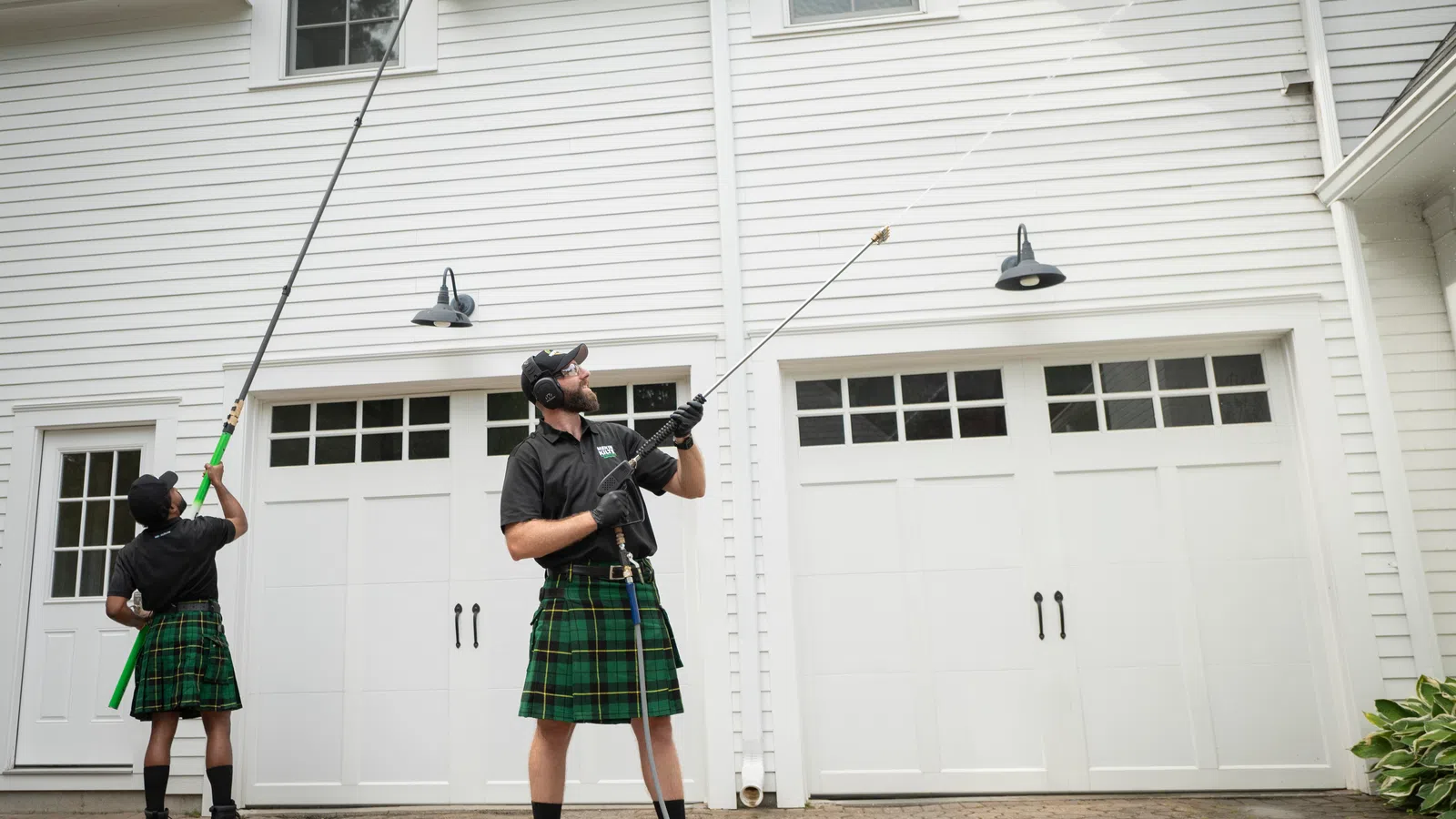 a person in a kilt holding a pressure washer in front of a white house