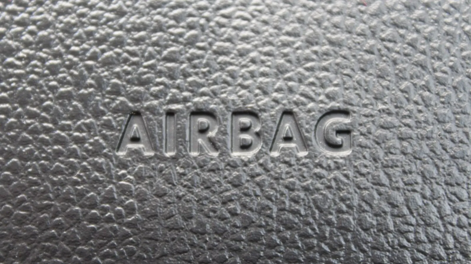 Close-up of embossed AIRBAG text on textured black car steering wheel material.