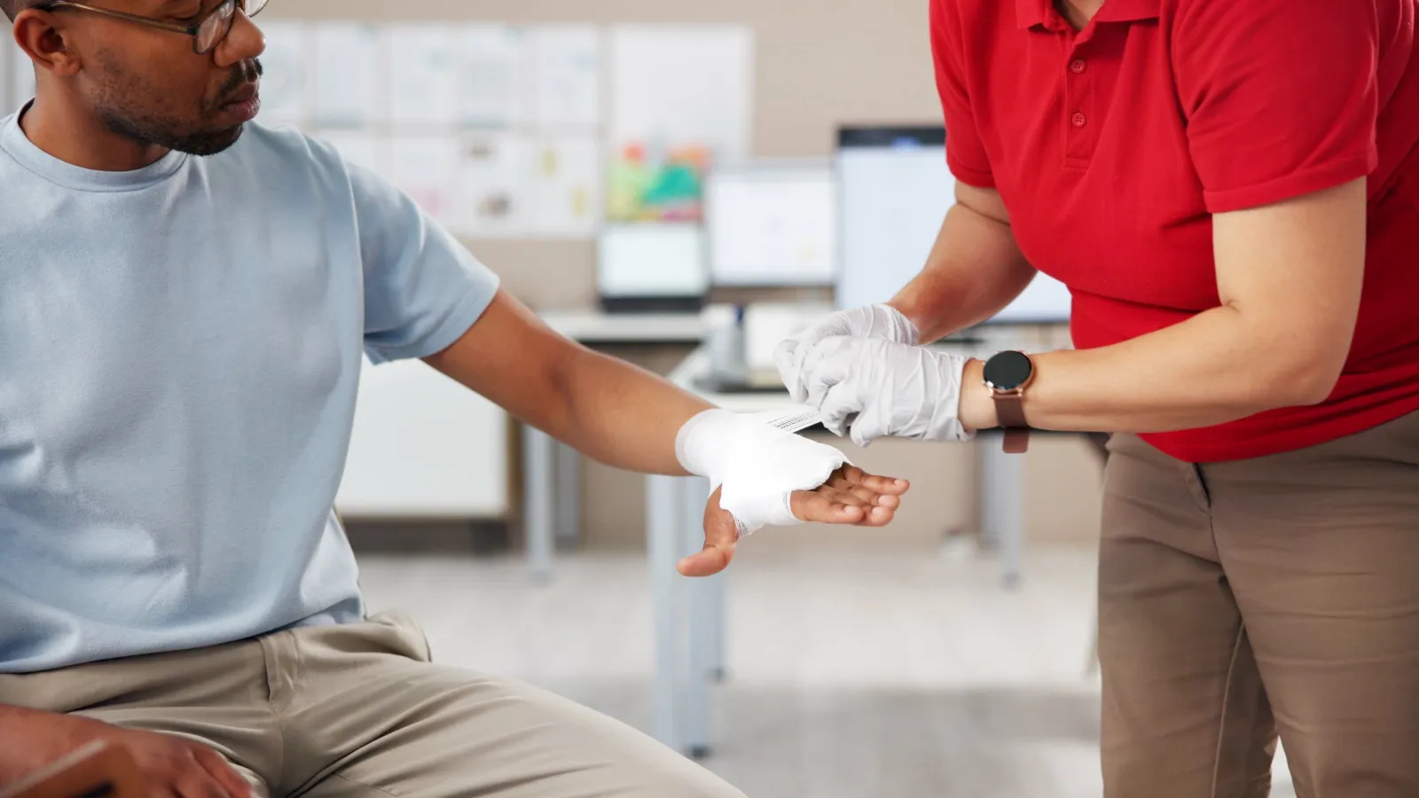 Person in blue shirt receiving first aid treatment with bandage applied to wrist indoors
