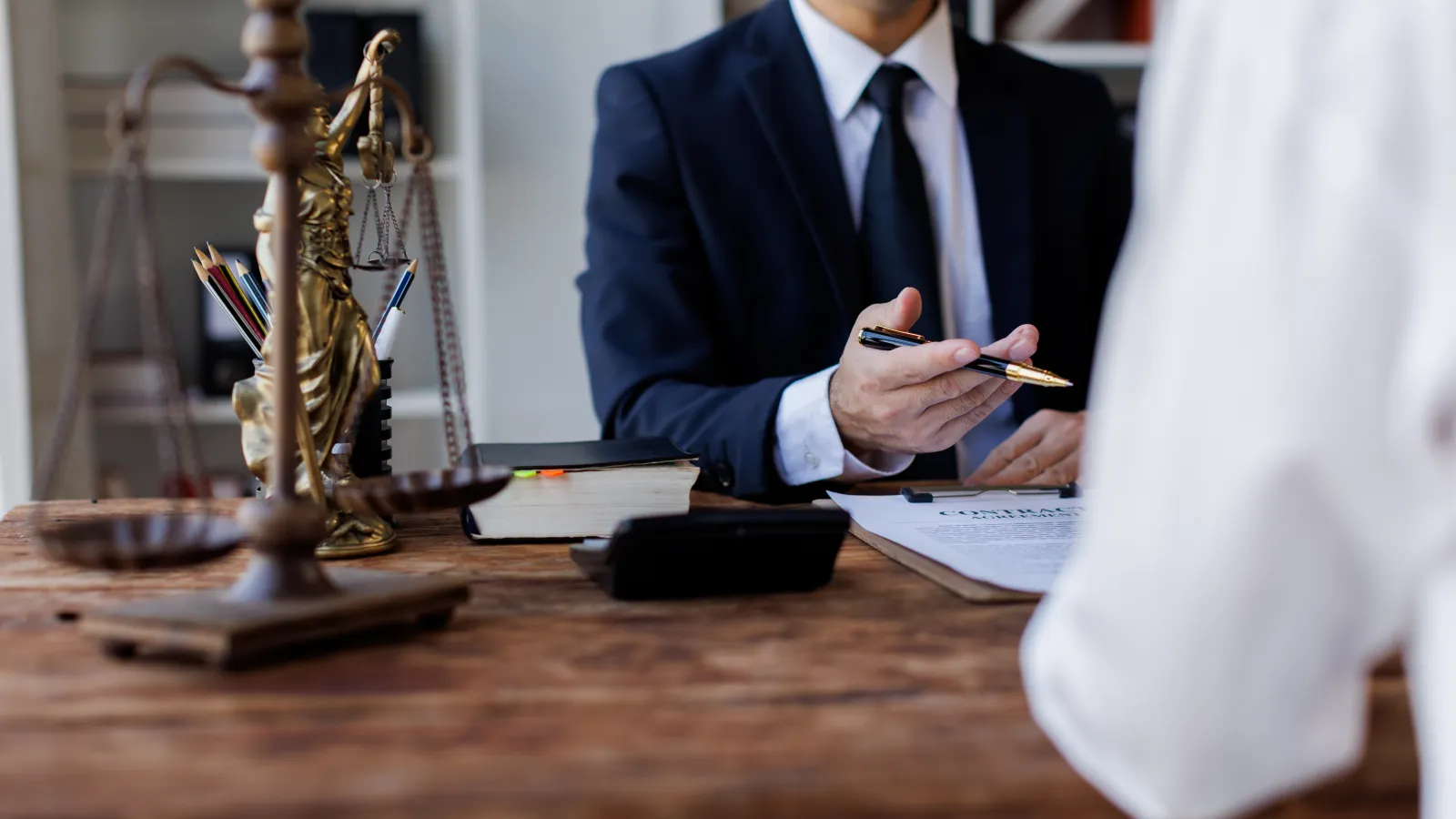 Lawyer in suit discussing legal documents with client in office featuring scales of justice on desk
