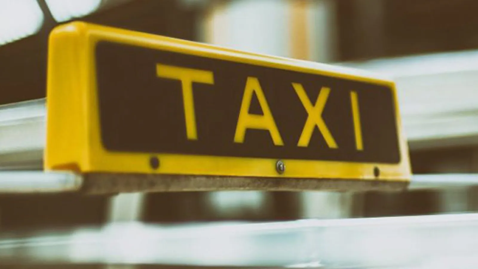 Close-up of a yellow and black taxi sign mounted on a vehicle roof against blurred background