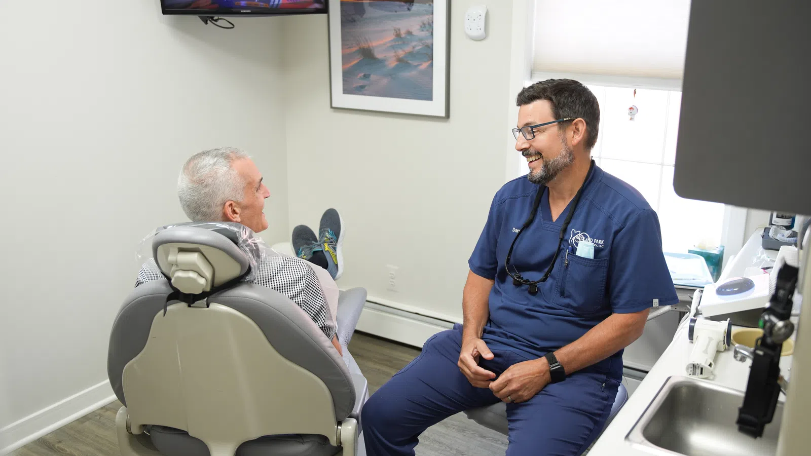 Dentist consulting and smiling with an elderly male patient in a modern dental clinic room.