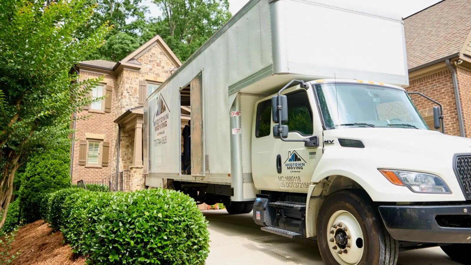 White Midtown Moving truck parked in driveway of a suburban brick house ready for moving service.