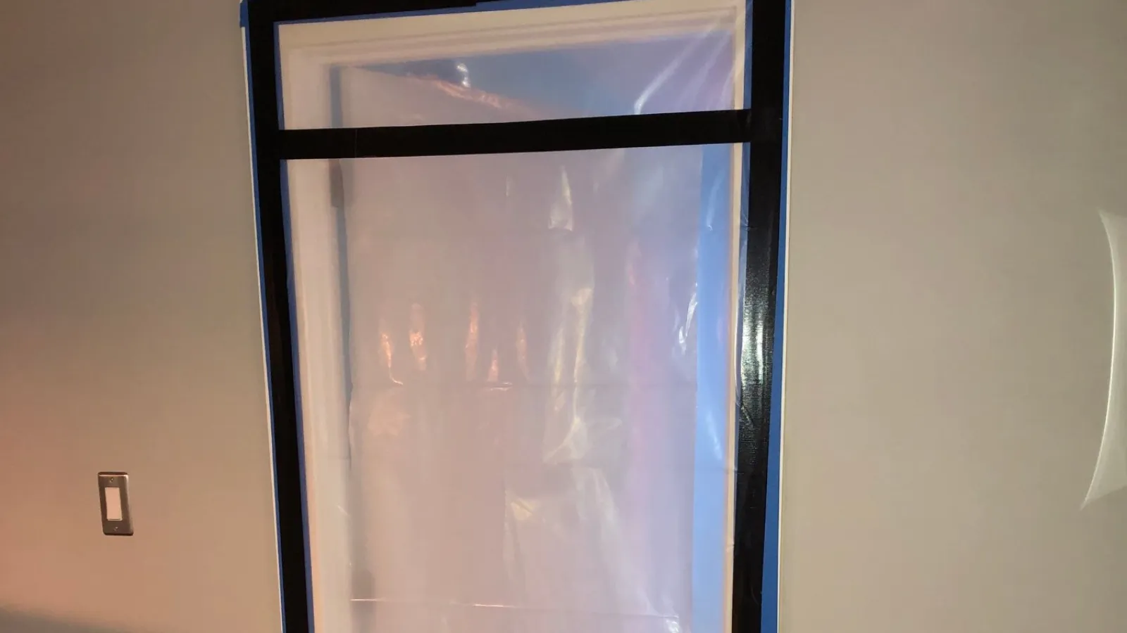 Temporary plastic door cover with black tape sealing indoors for dust or smoke containment during construction or renovation.