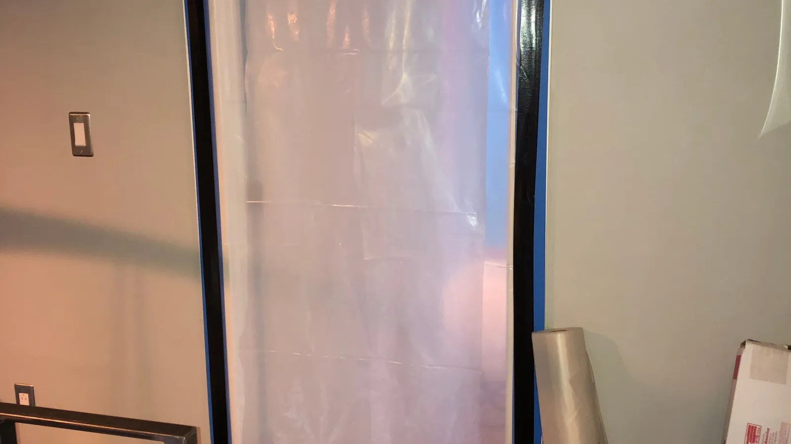 Clear plastic sheet taped to door frame with black tape, protecting floor and room during renovation work.
