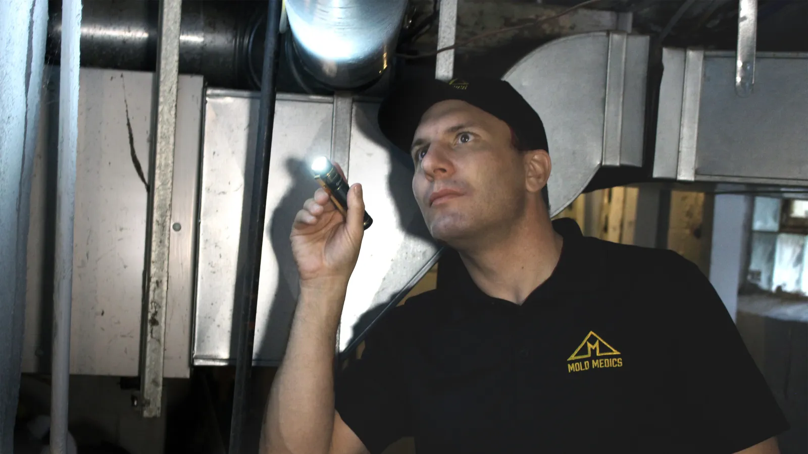Technician inspecting industrial HVAC ductwork with flashlight in a building basement