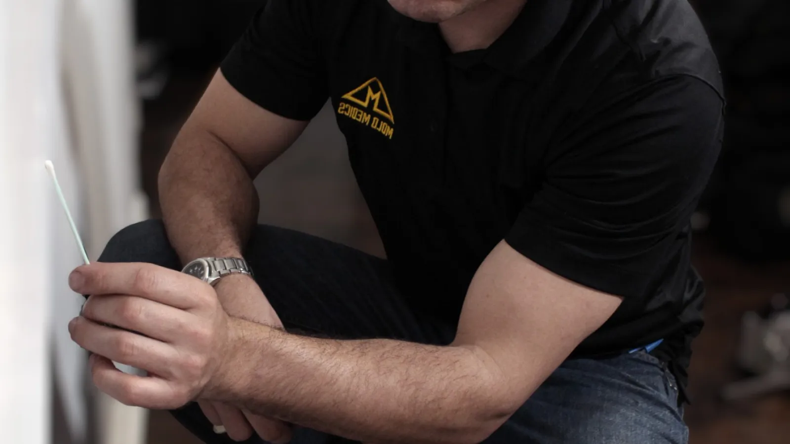 Technician wearing Mold Medics uniform inspecting a wall for mold with a testing swab inside a home.