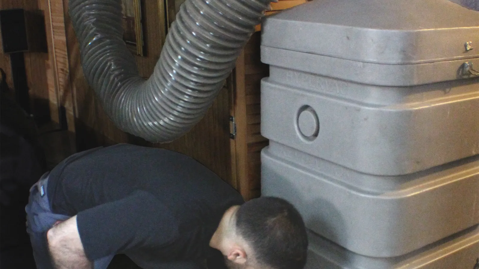 Man connecting large air purifier or ventilation unit with flexible duct hose inside a room.