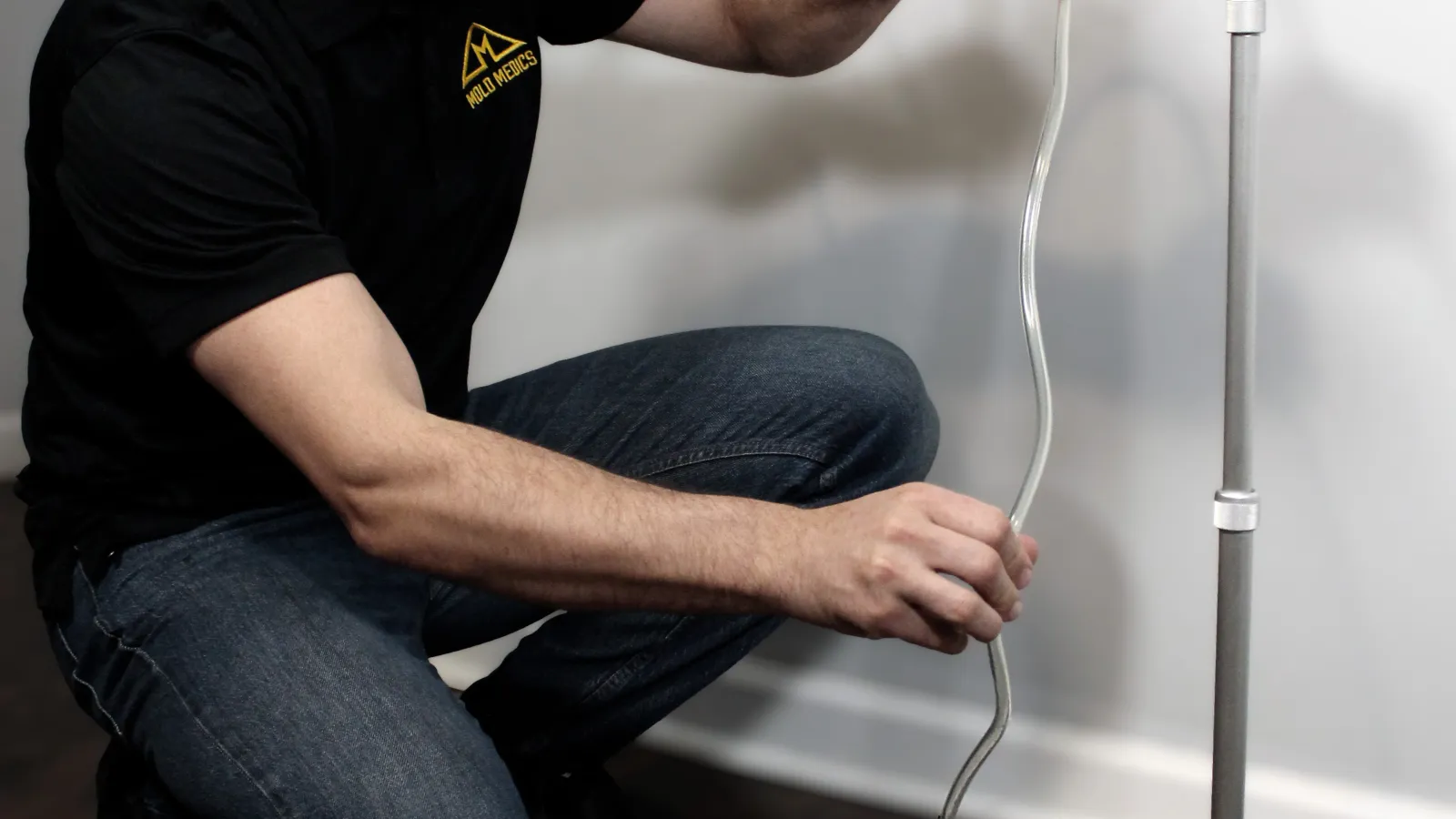 Technician wearing Mold Medics uniform sets up air quality testing equipment indoors on wooden floor.