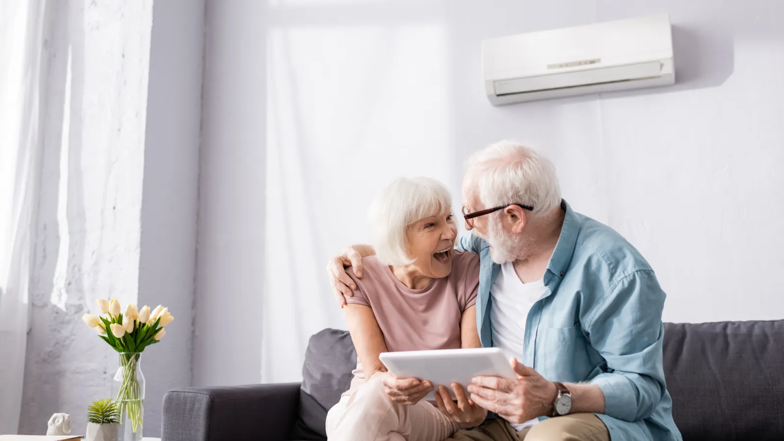 Happy elderly couple sitting on couch using a tablet together in a bright modern living room
