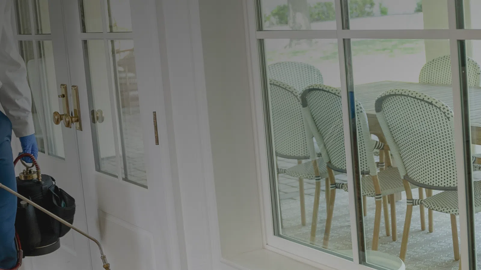 Pest control professional spraying insecticide inside a home near sliding glass doors to a patio.