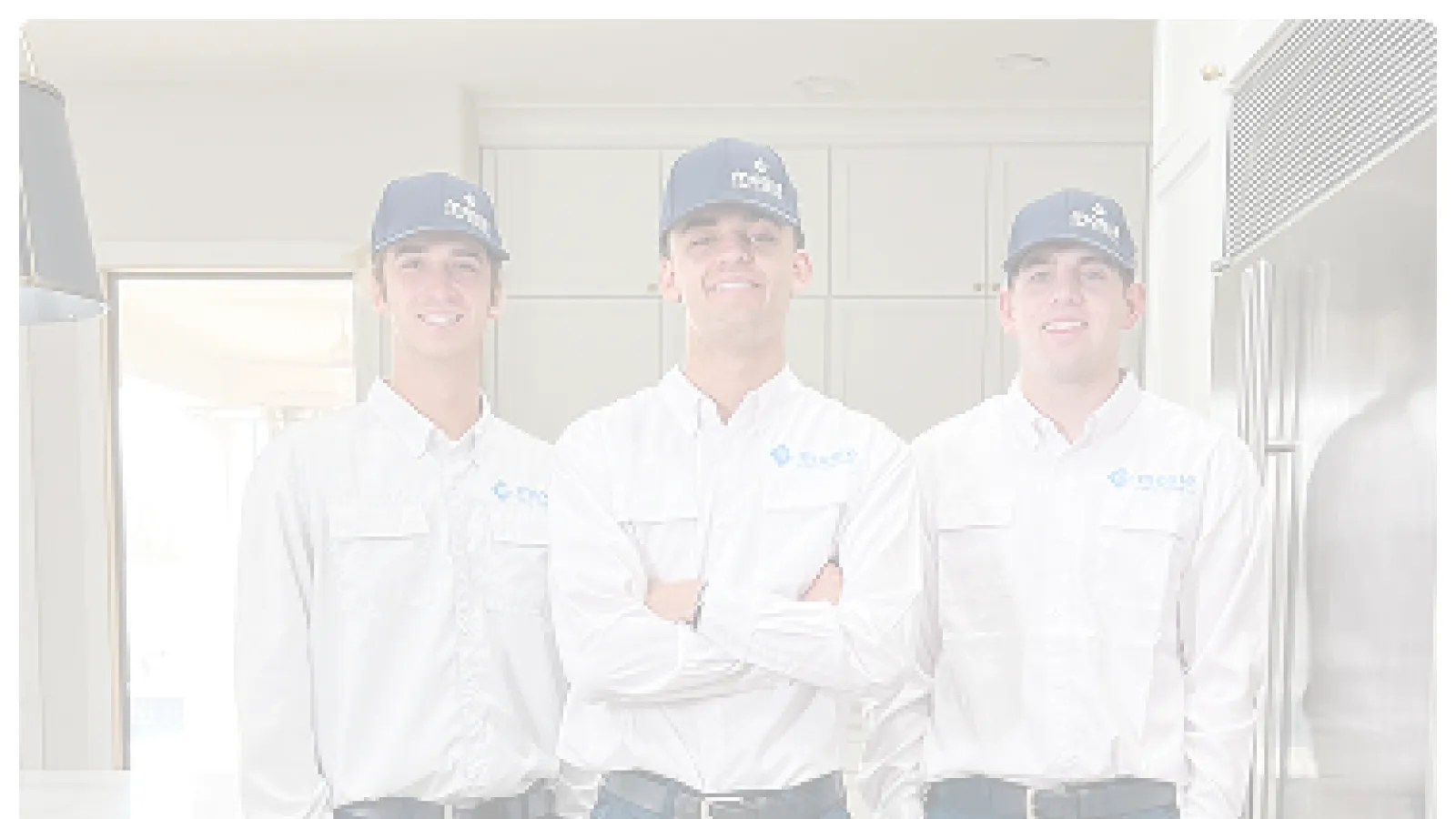 Three uniformed technicians wearing white shirts and blue pants standing in a modern kitchen.