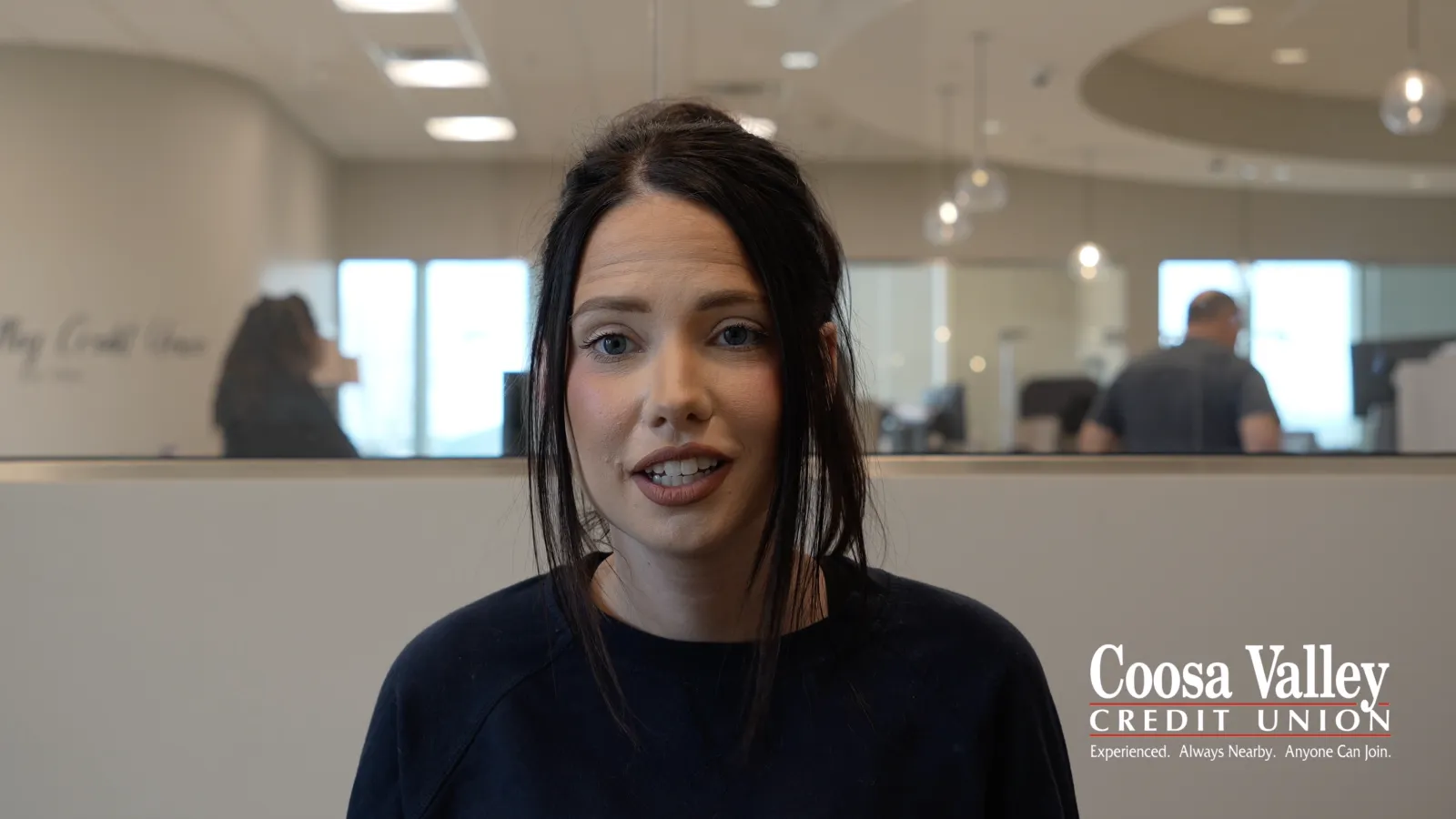 Young woman speaking in a modern office setting with Coosa Valley Credit Union logo visible.