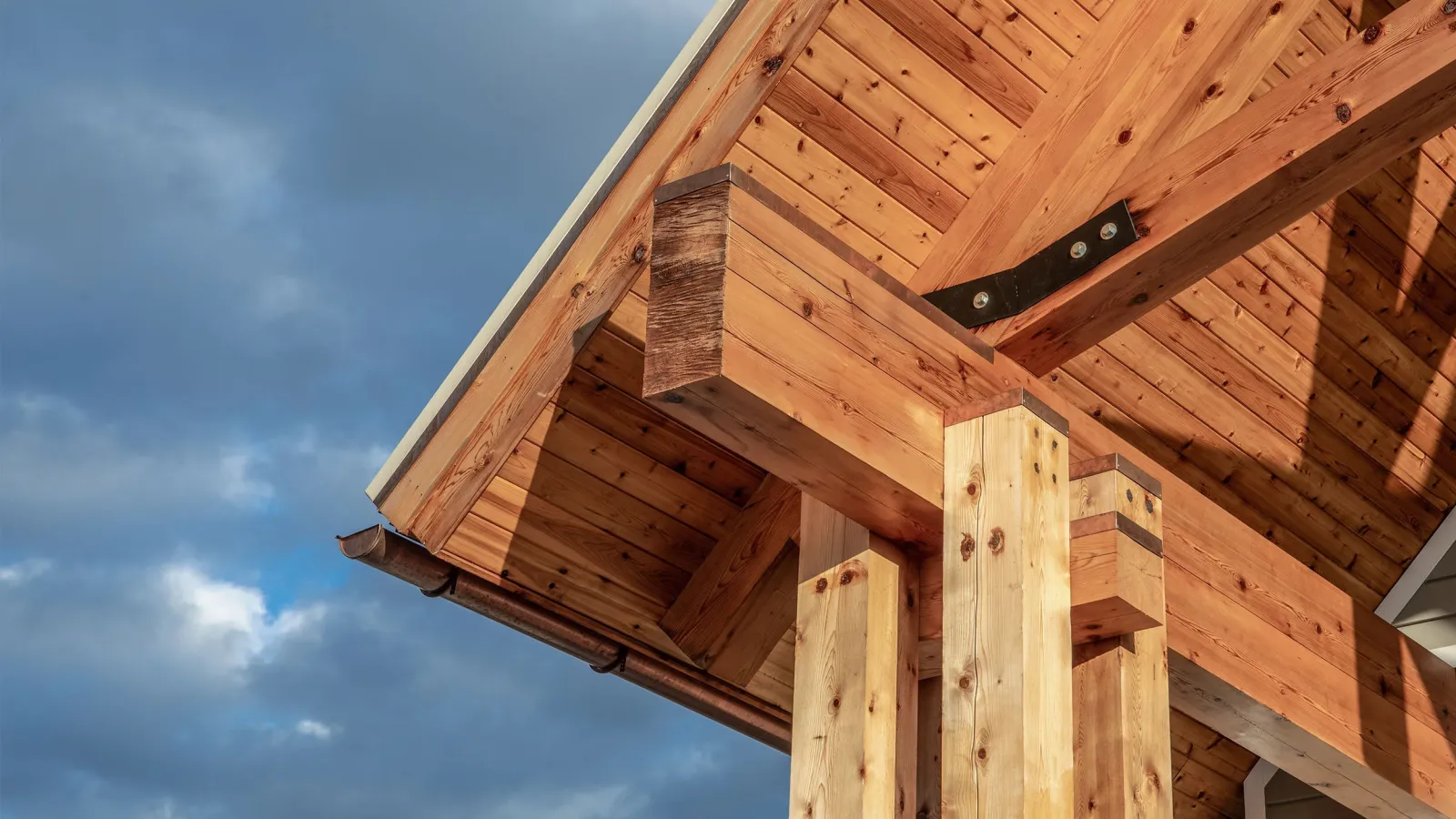 Close-up of wooden beams and roof structure with metal bolts under a cloudy sky.